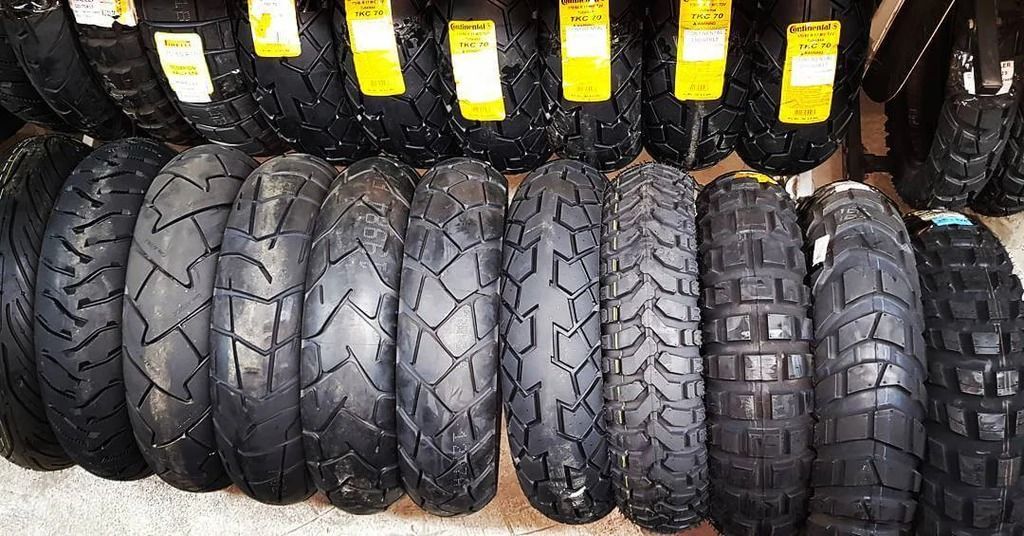 Filas de neumáticos de motocicleta con distintos patrones de banda de rodadura, exhibidos en un entorno de tienda.