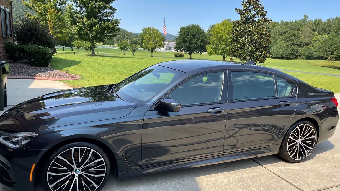 A black bmw is parked in a driveway next to a grassy field.