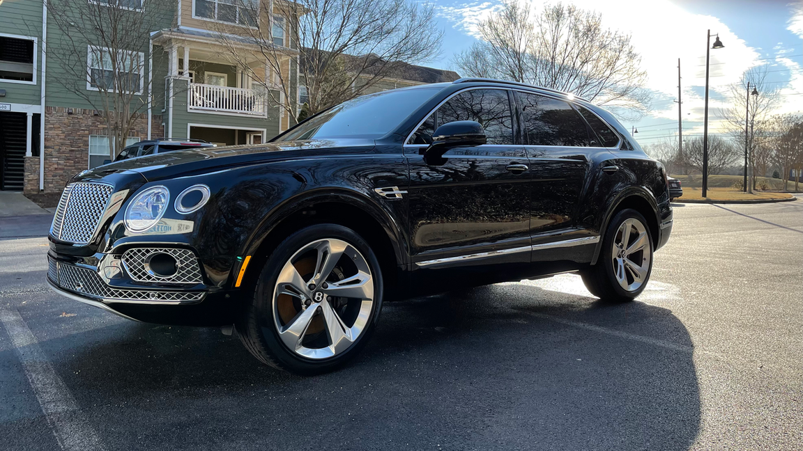 A black bentley is parked in a parking lot in front of a building.