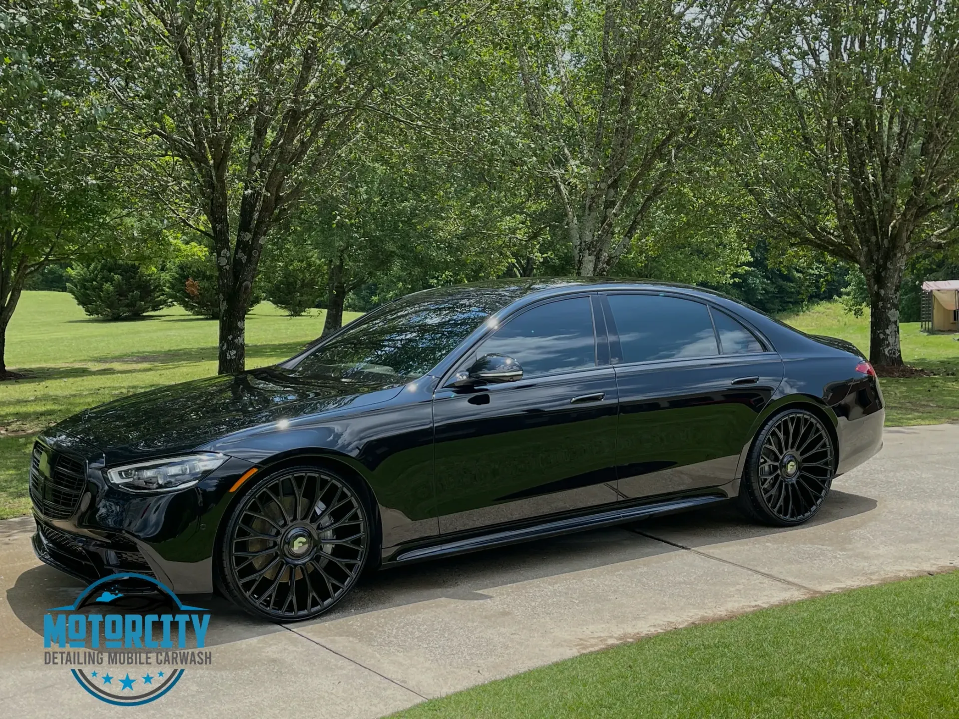 A black car is parked on a sidewalk in front of trees.
