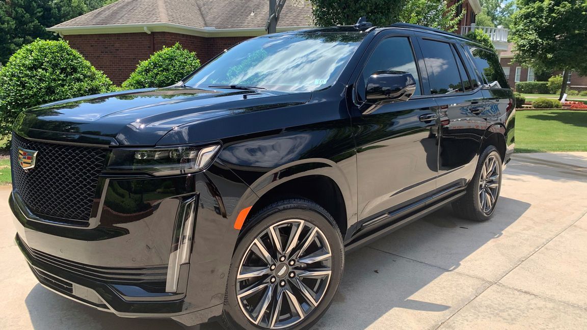 A black cadillac escalade is parked in a driveway in front of a house.