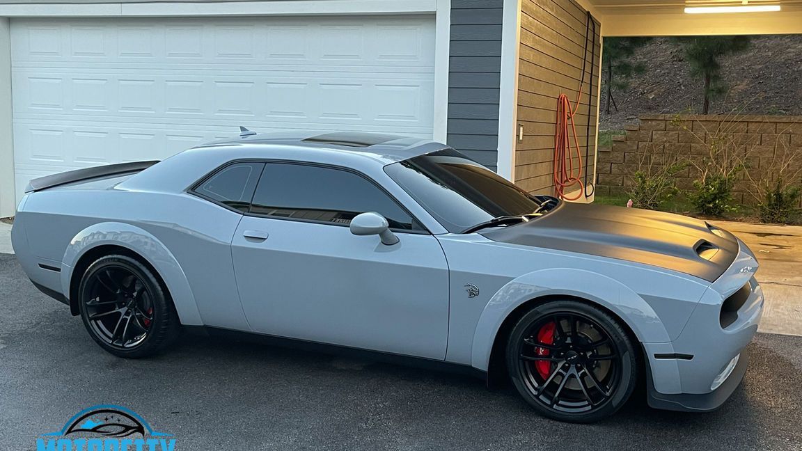 A gray dodge challenger is parked in front of a garage door.