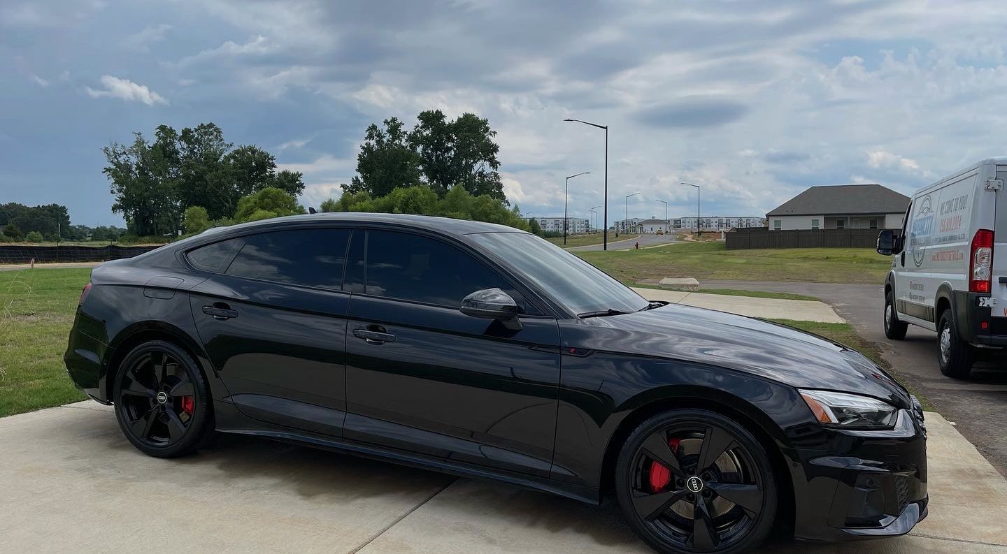 A black car is parked in a driveway next to a truck.