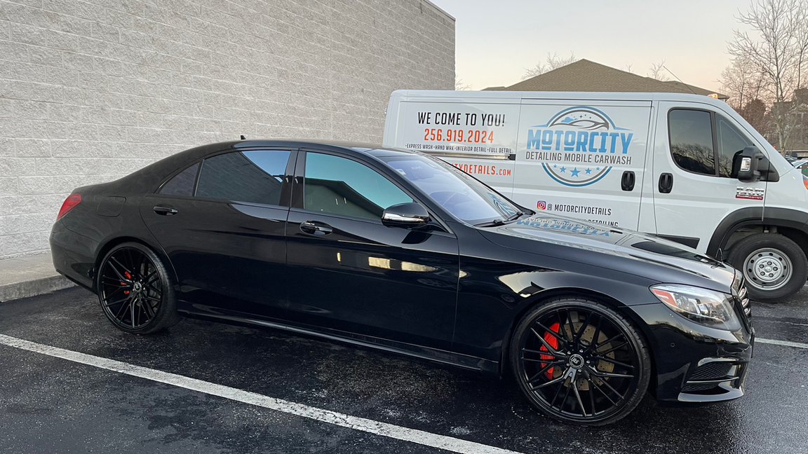 A black car is parked next to a white van in a parking lot.