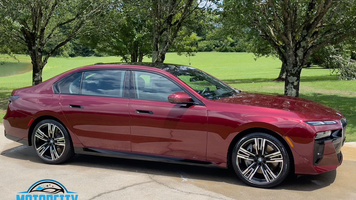 A red car is parked in a driveway next to trees.