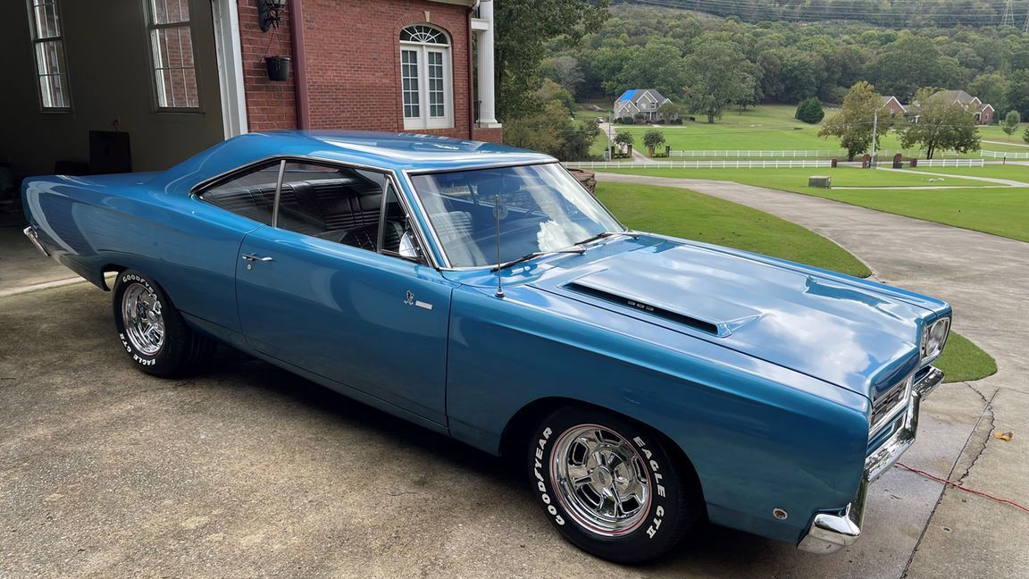 A blue muscle car is parked in a driveway in front of a garage.