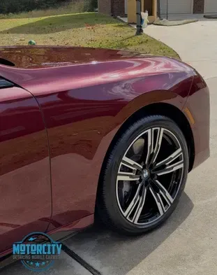 A red car is parked in a driveway next to a house.