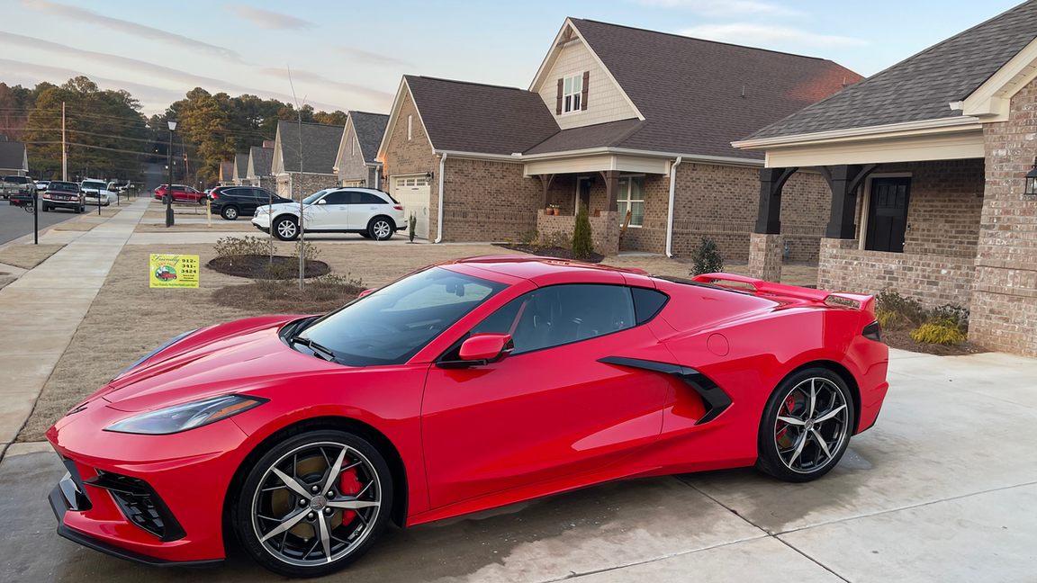 A red sports car is parked in front of a brick house.