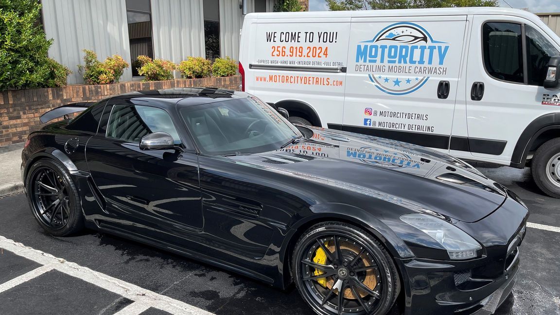 A black sports car is parked in a parking lot next to a white van.
