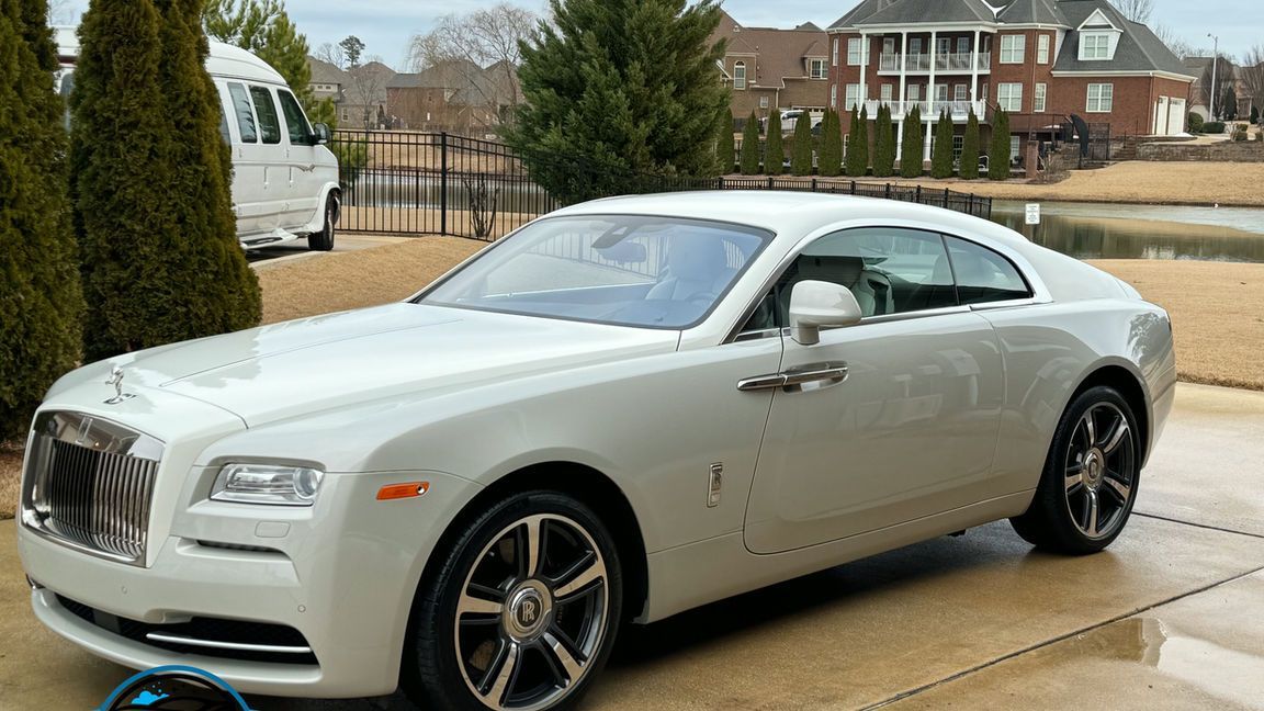 A white rolls royce is parked in a driveway next to a house.