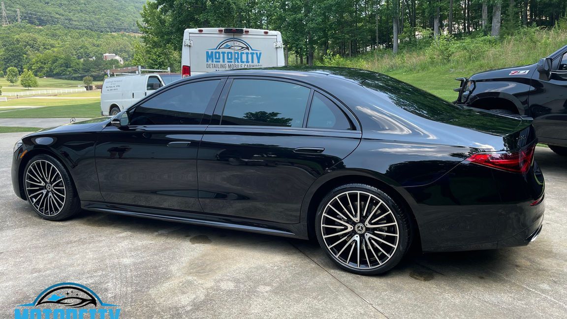 A black car is parked in a parking lot next to a truck.