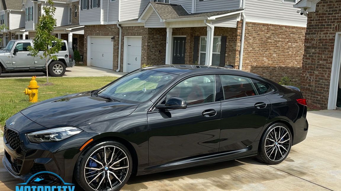 A black car is parked in front of a brick house.