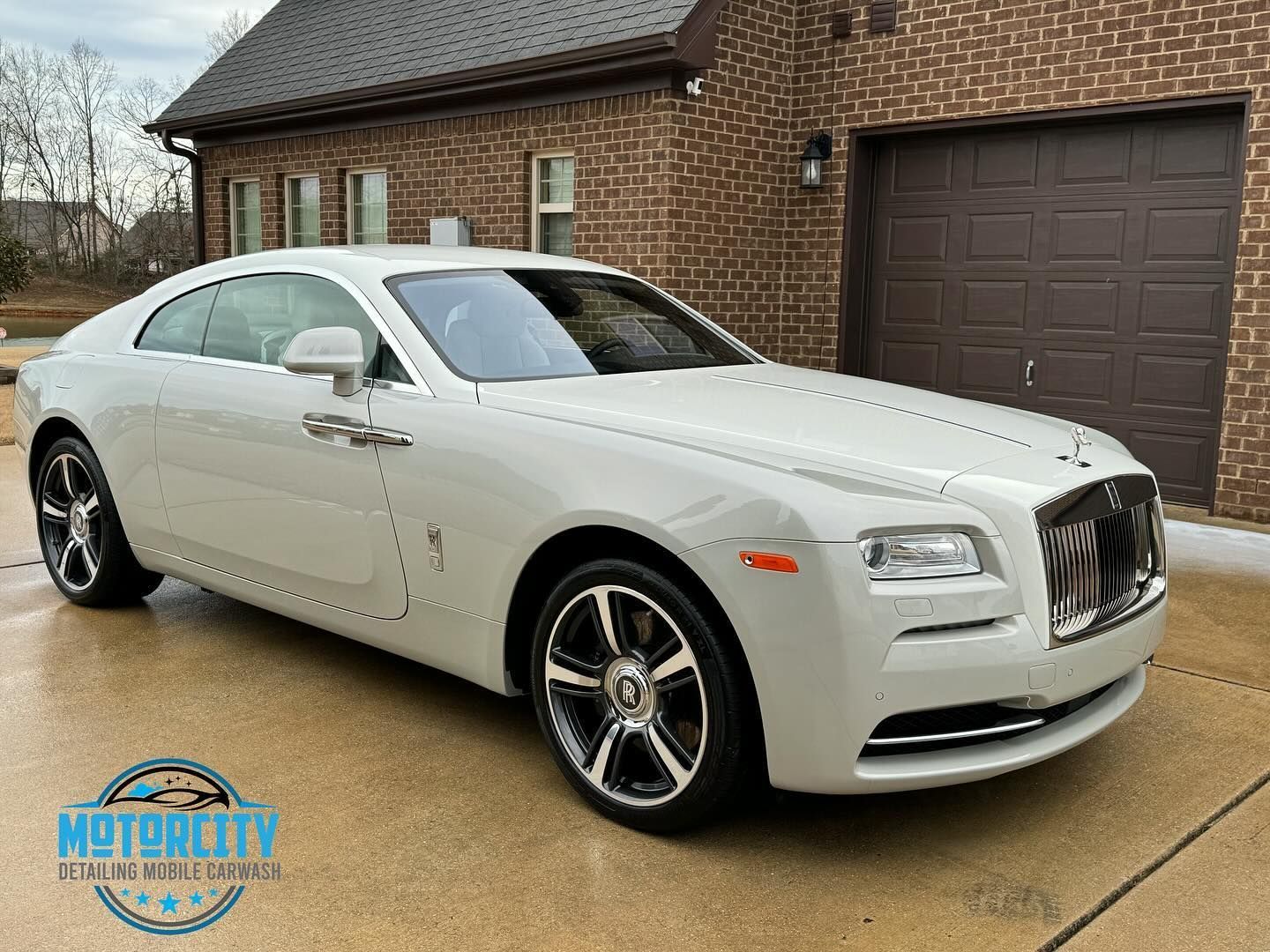 A white rolls royce rr is parked in front of a brick house.
