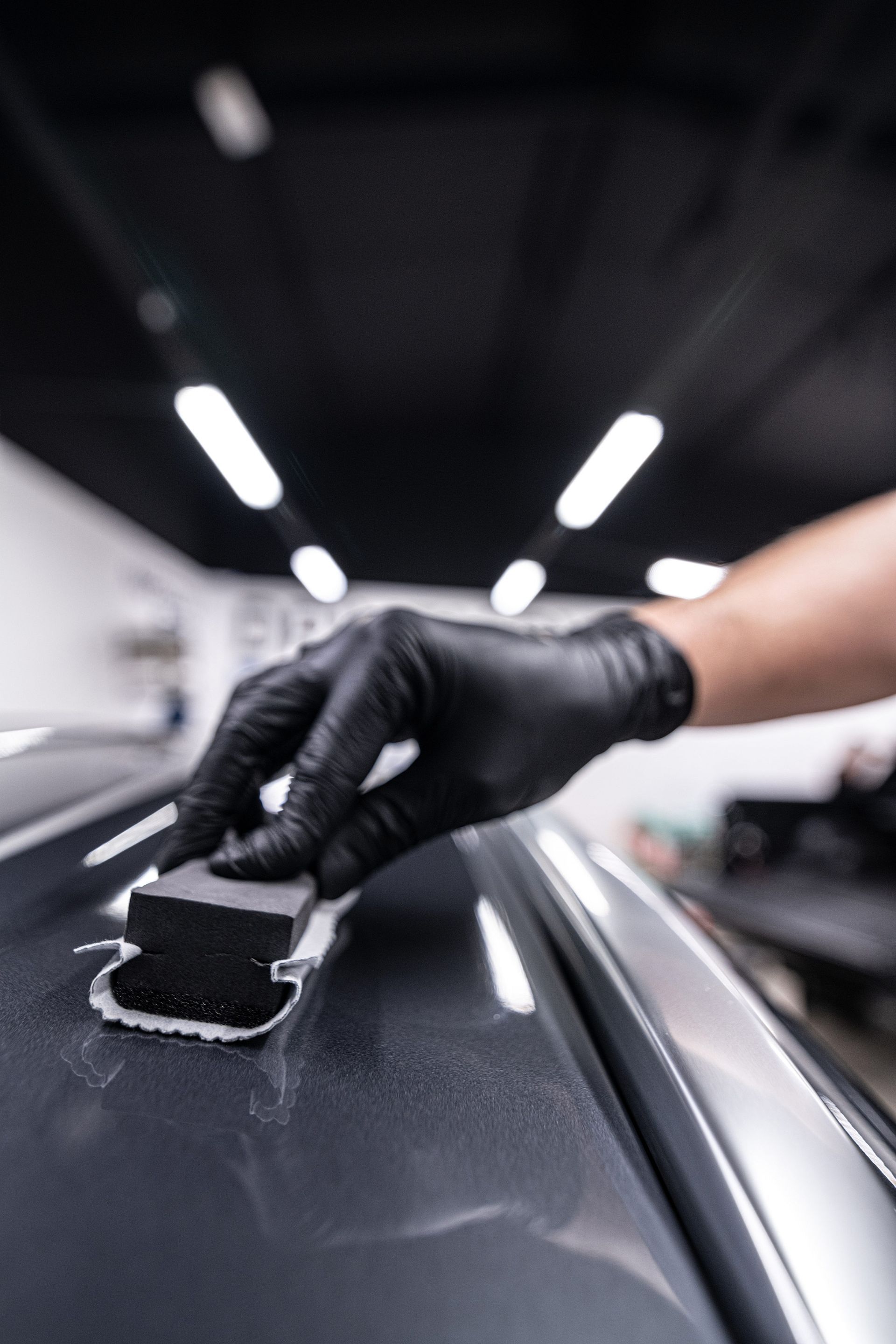 A person wearing black gloves is polishing the hood of a car.
