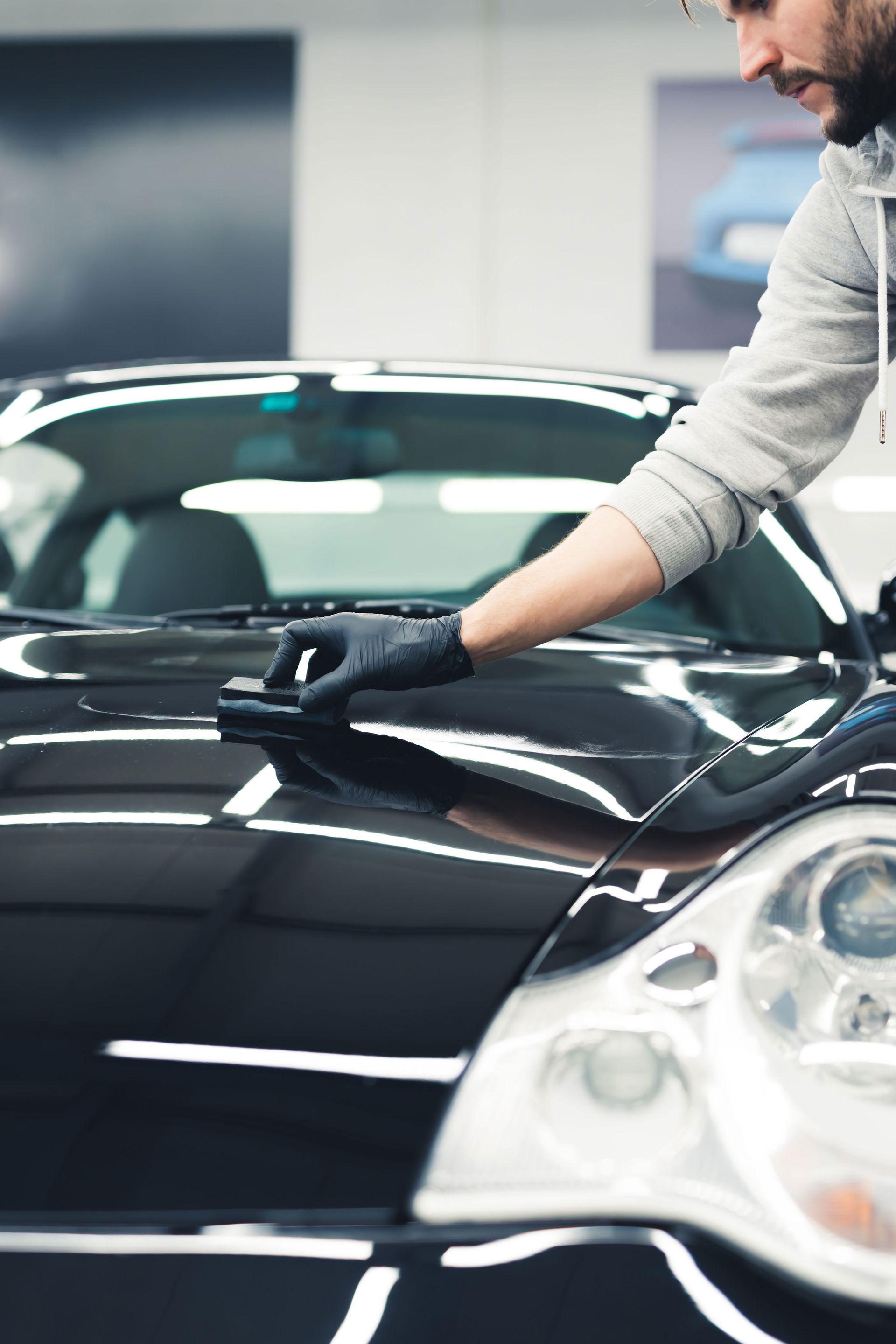 A person is polishing a black car with a sponge.