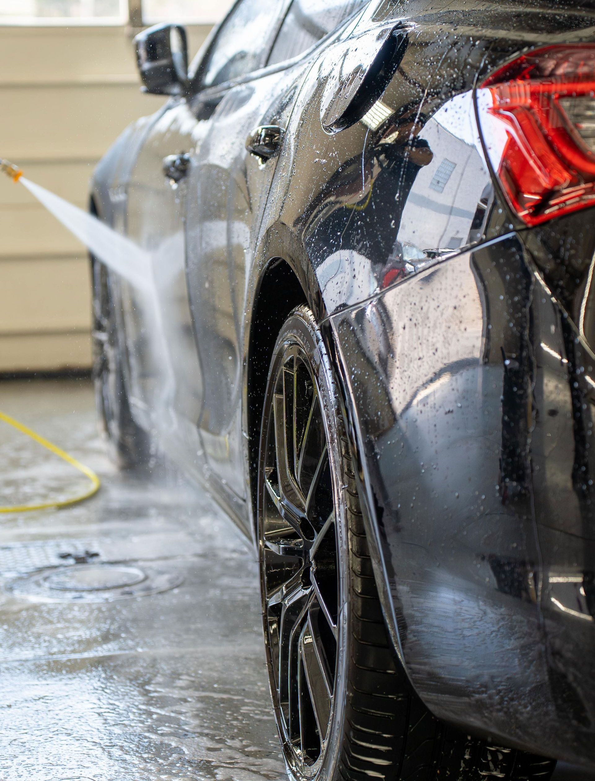 A car is being washed with a high pressure washer in a garage.