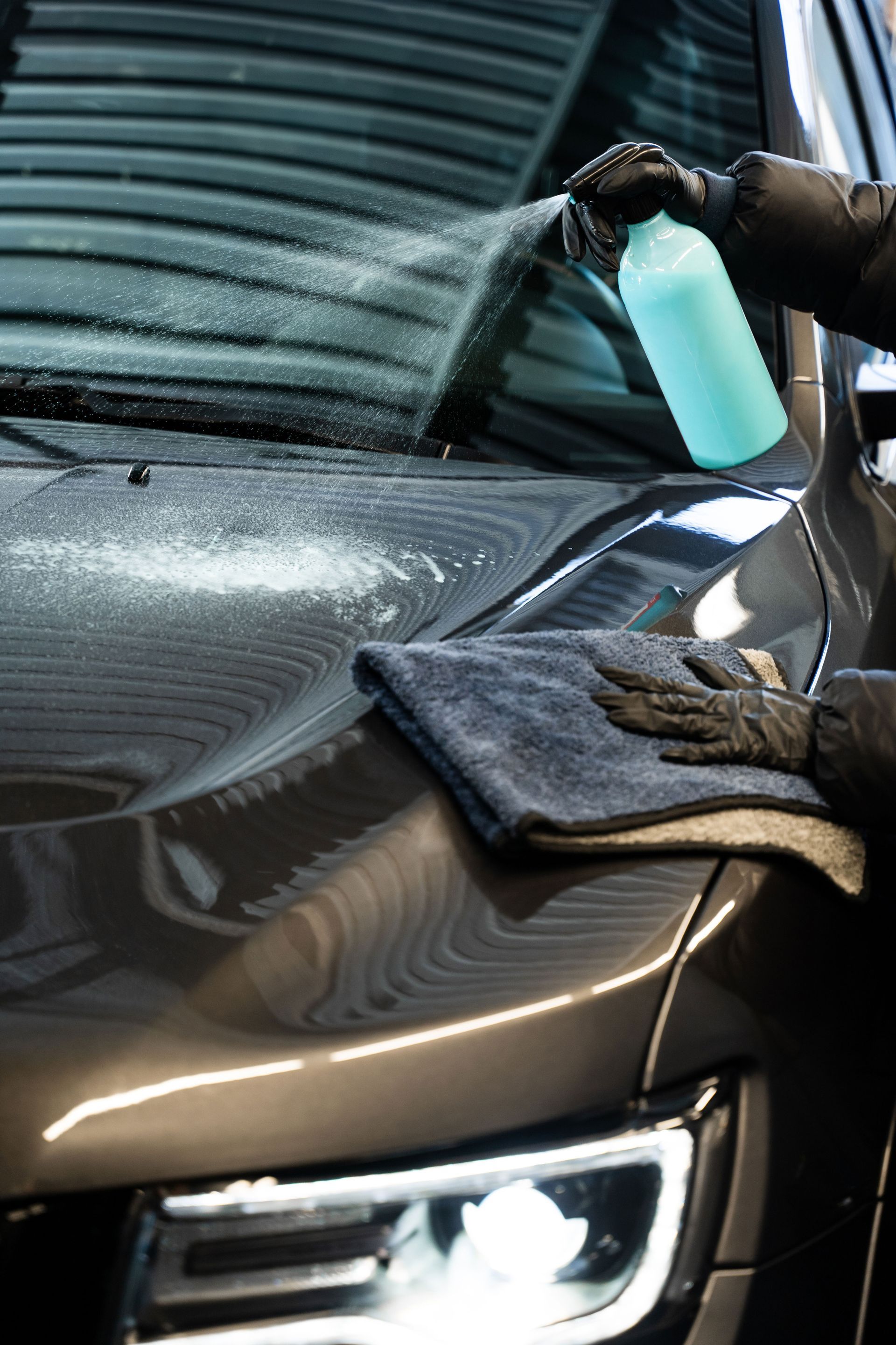 A person is cleaning a car with a towel and spray bottle.