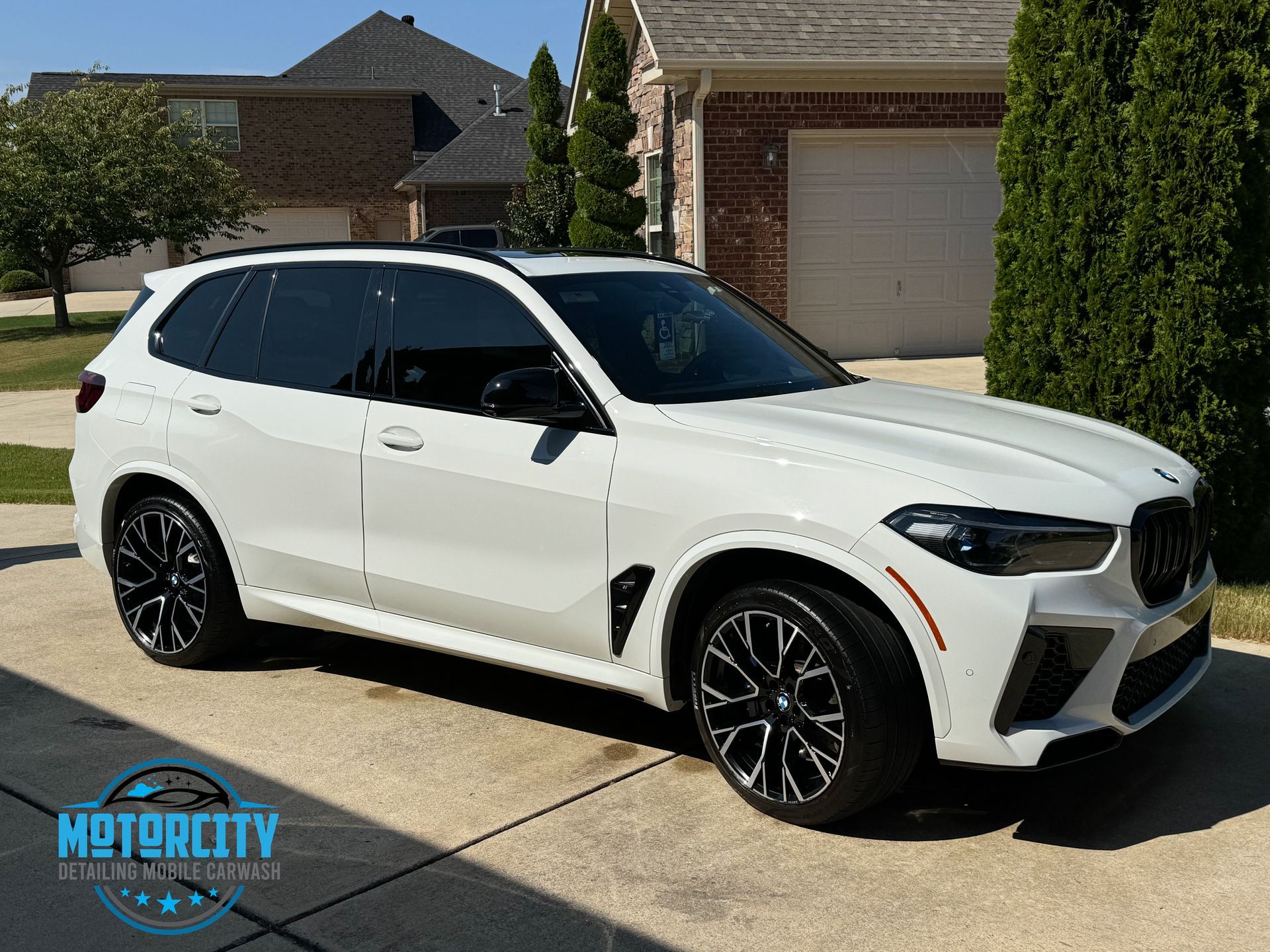 A white bmw x5 m is parked in front of a brick house.