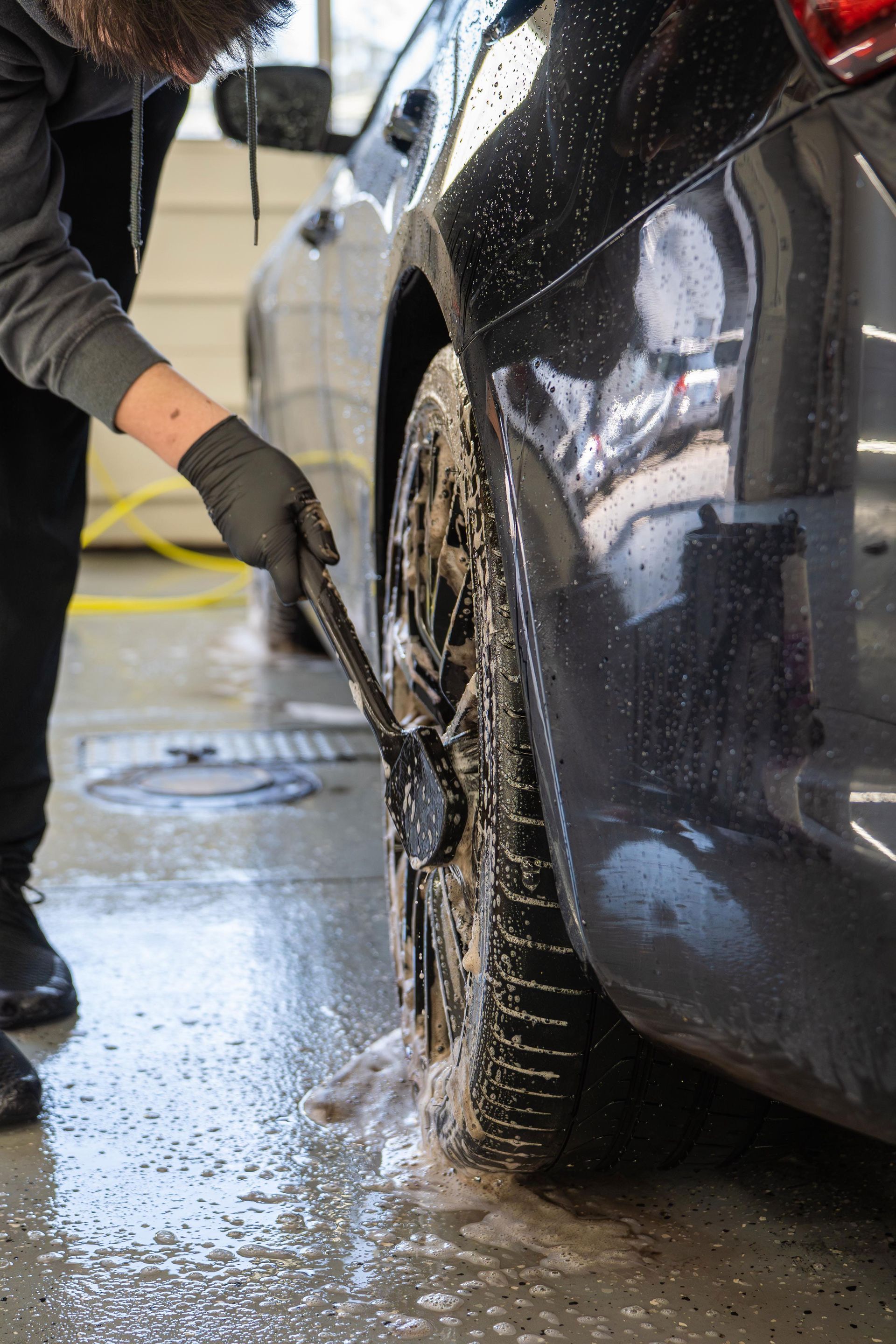 A man is washing a car with a brush in a garage.