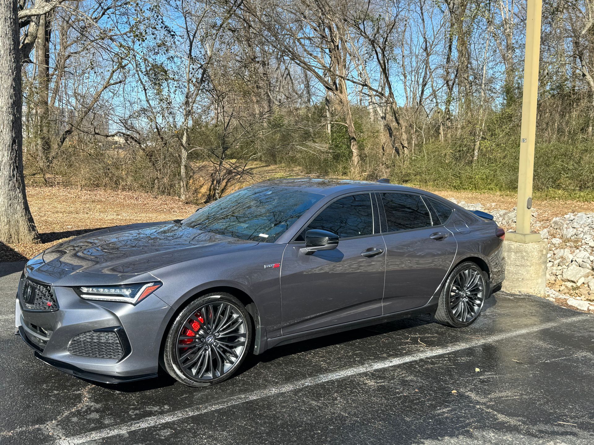 A gray car is parked in a parking lot with trees in the background.
