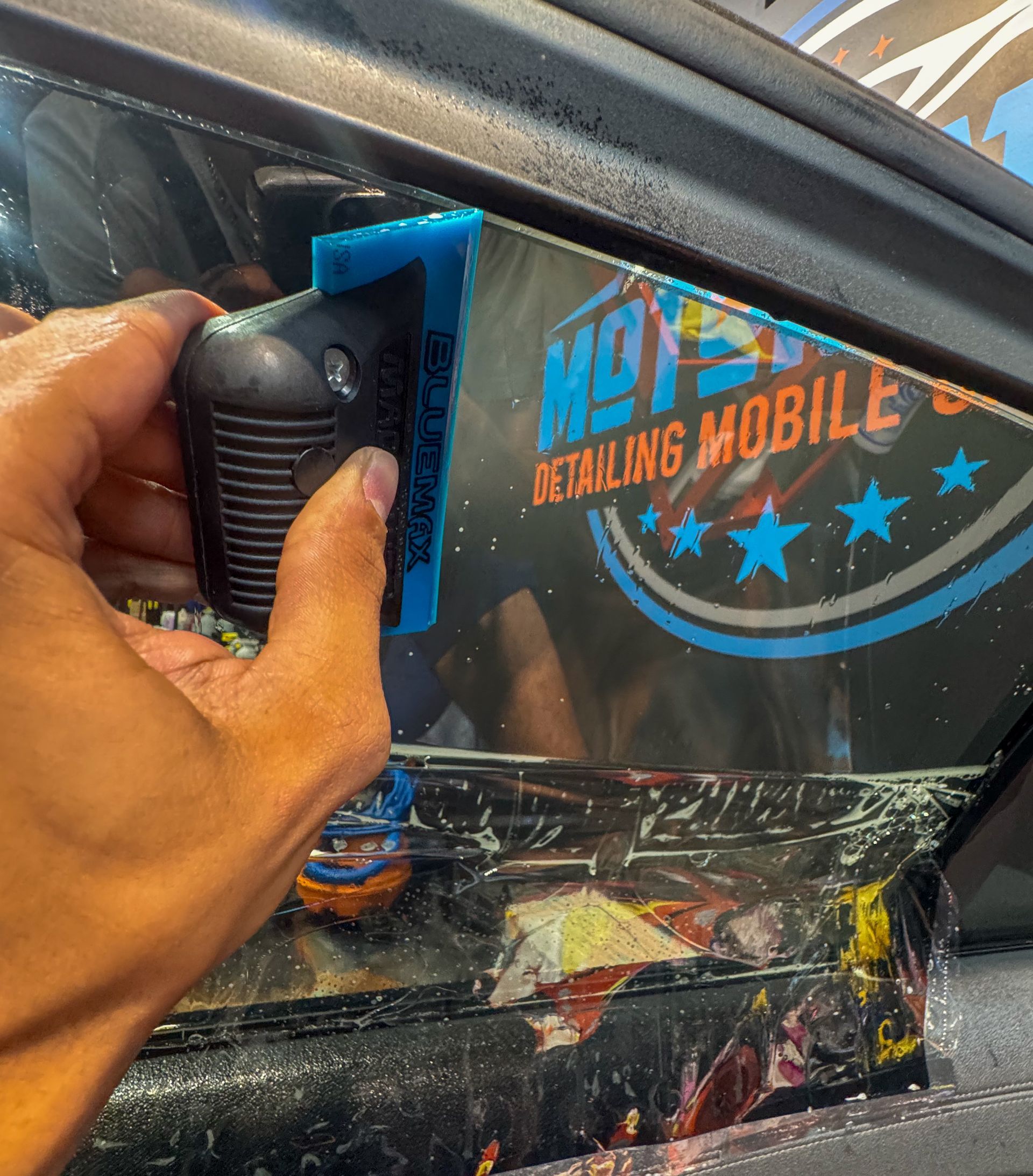 Person using a squeegee to apply window tint to a car window.