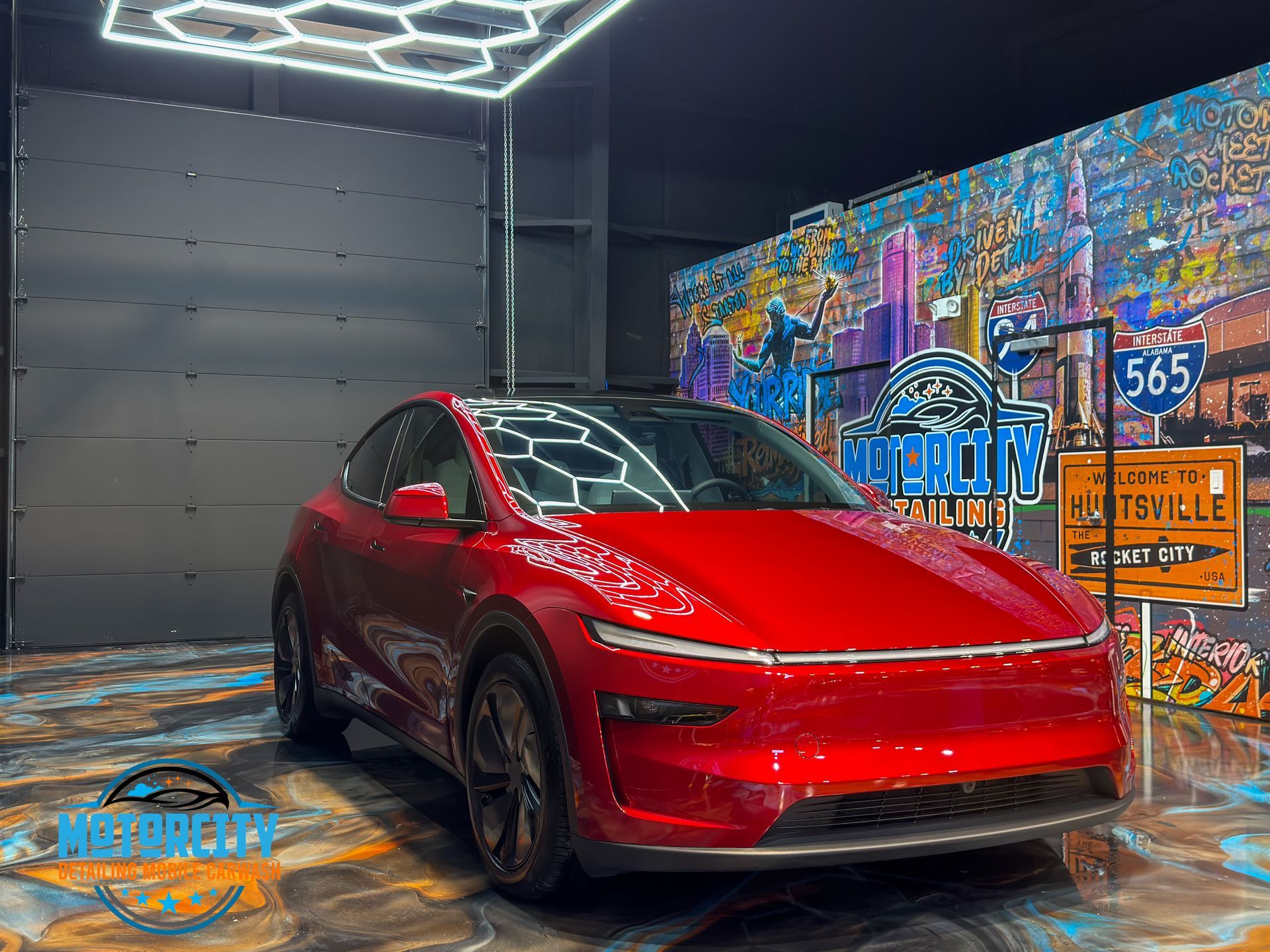Red electric vehicle parked in front of a colorful mural inside a modern garage setting.