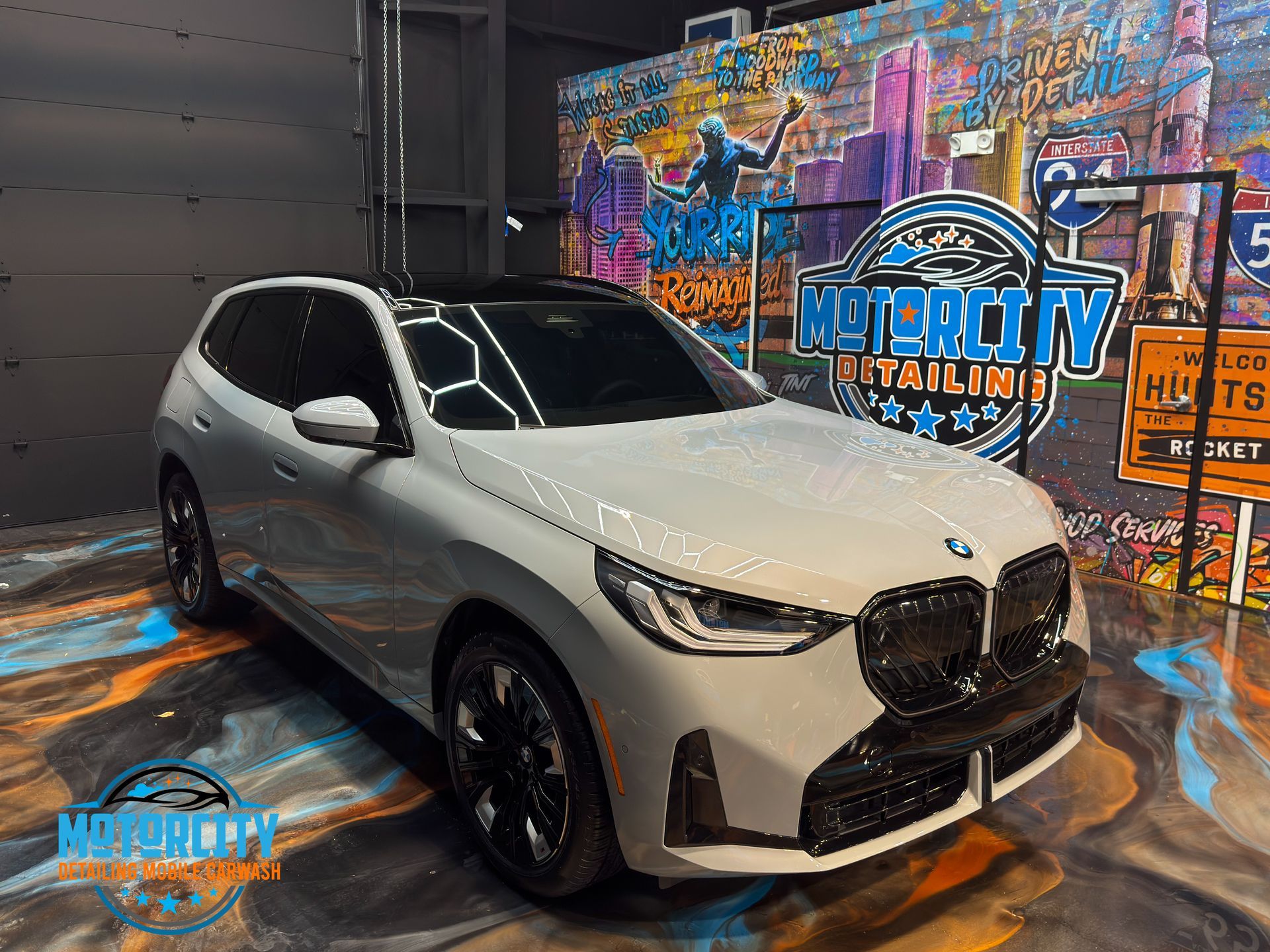 White BMW SUV with black accents in front of a colorful mural in a studio setting.