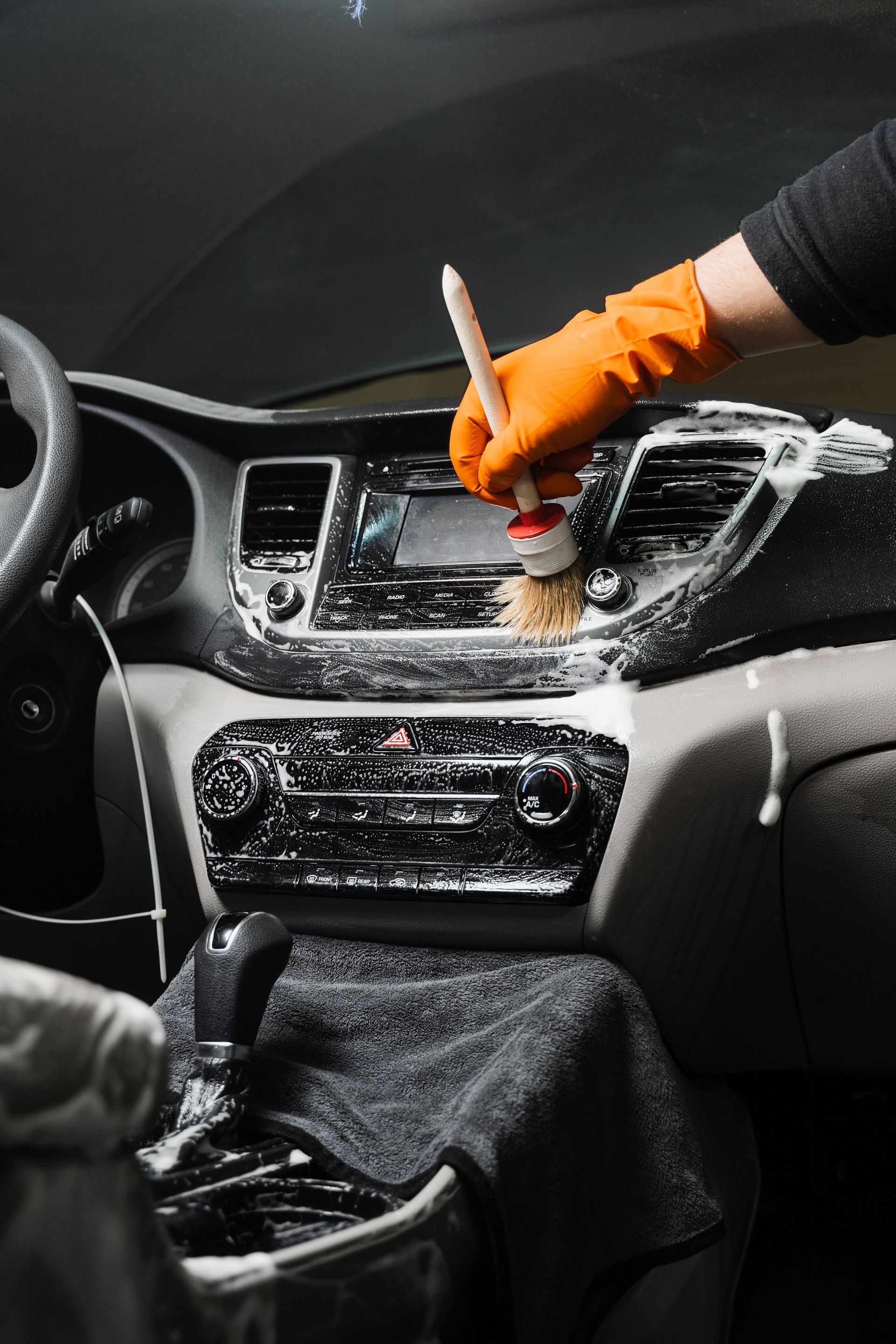 A person is cleaning the dashboard of a car with a brush.