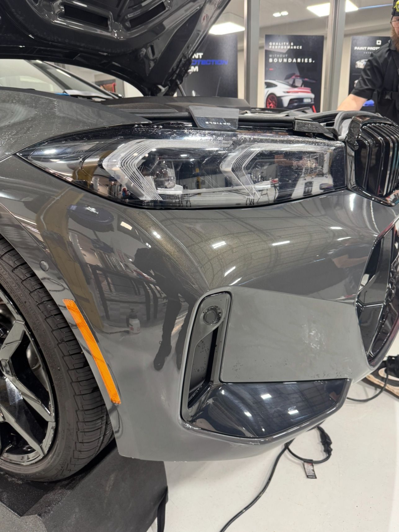 A man is working on the front of a car with the hood open.