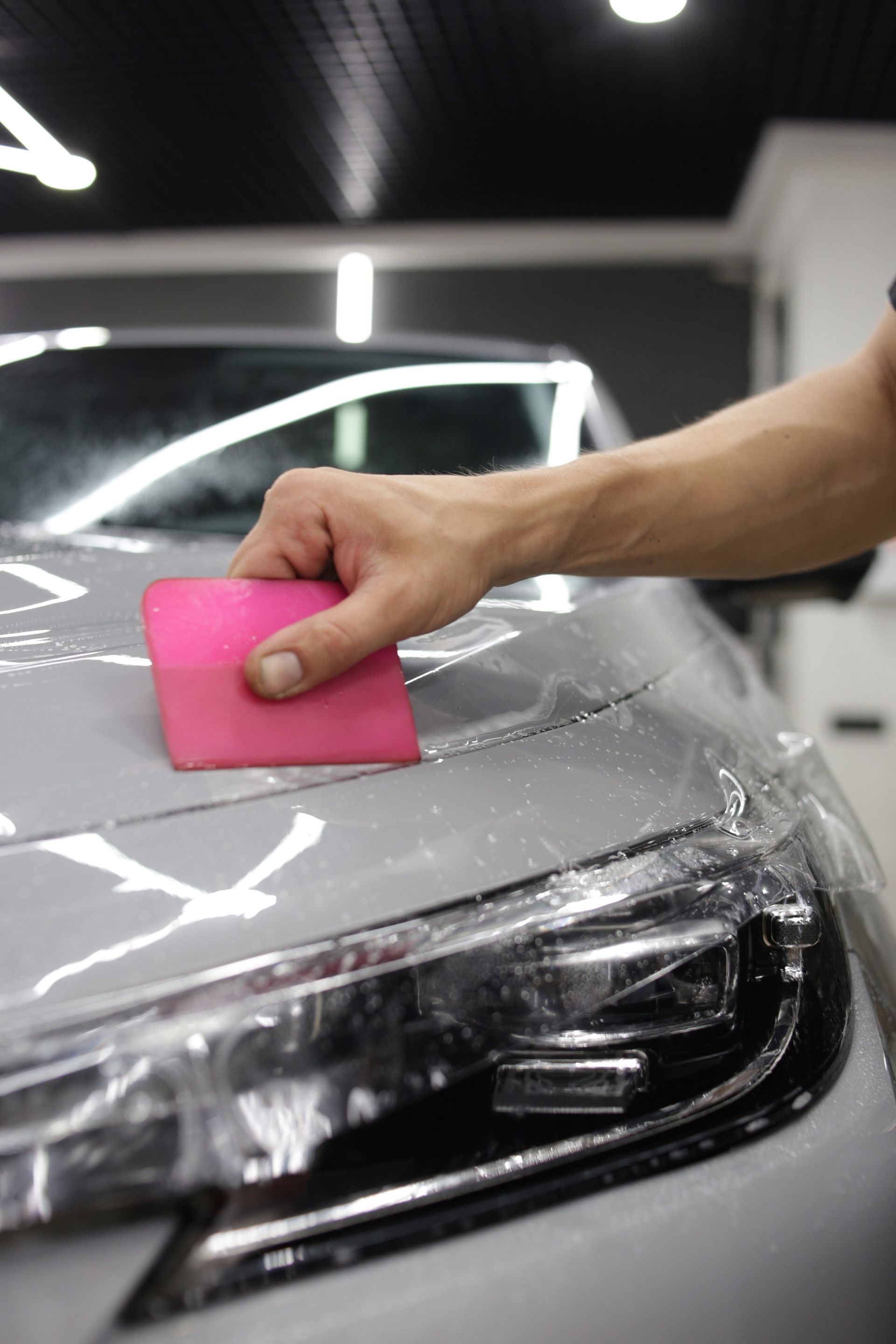 A person is applying protective film to the hood of a car.