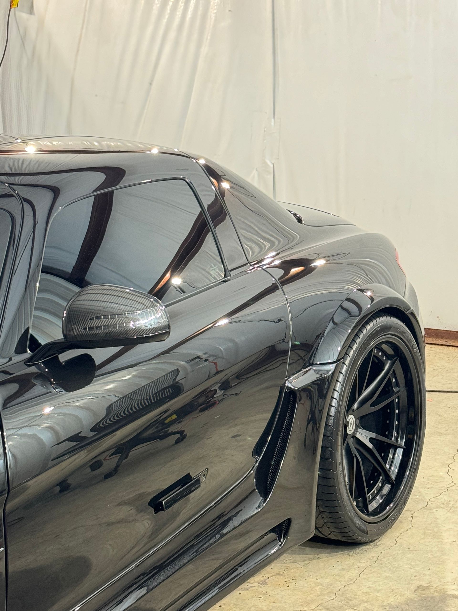 A person is polishing a black car with a sponge.