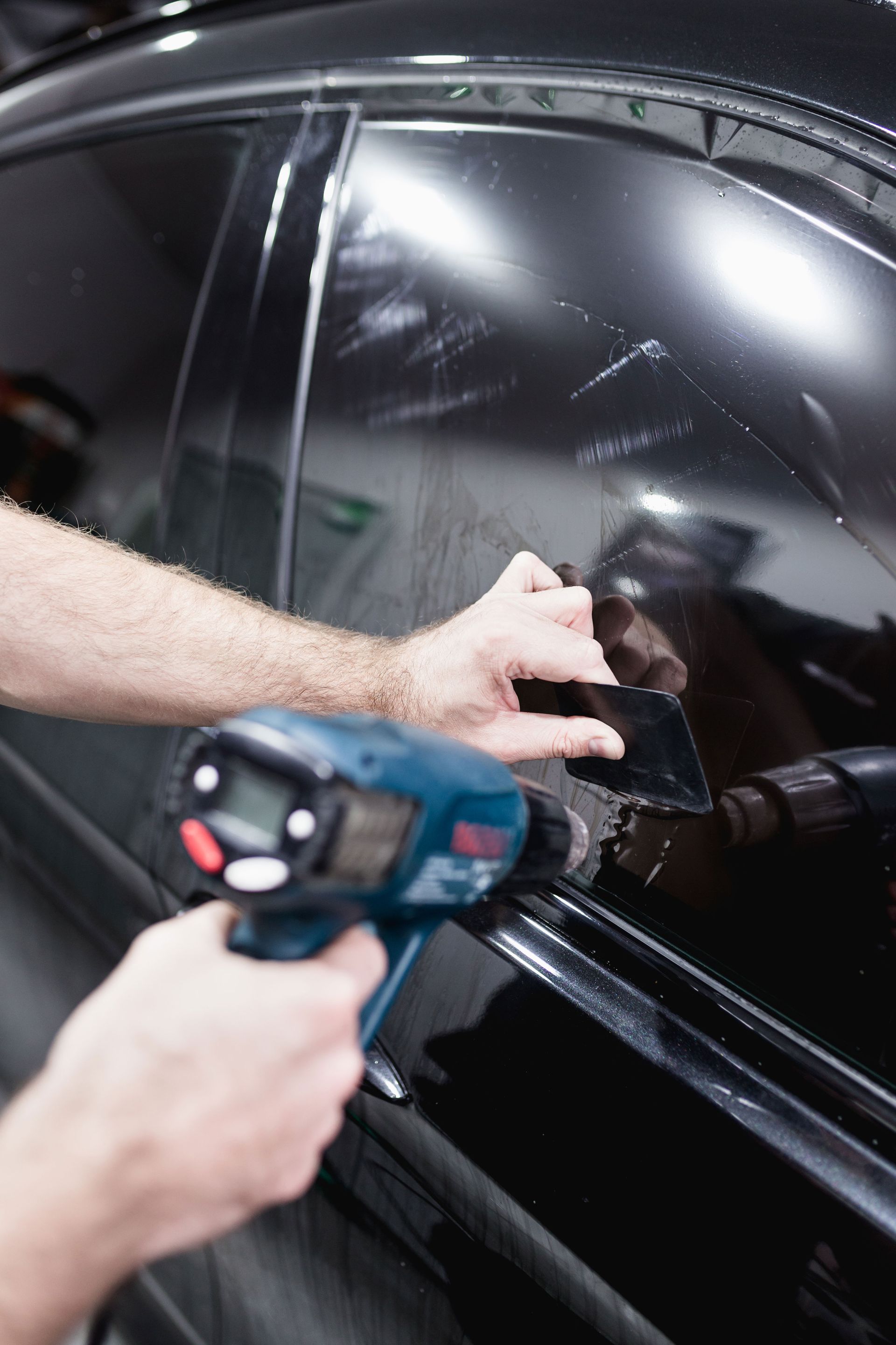 A man is applying tinted window film to a car window.