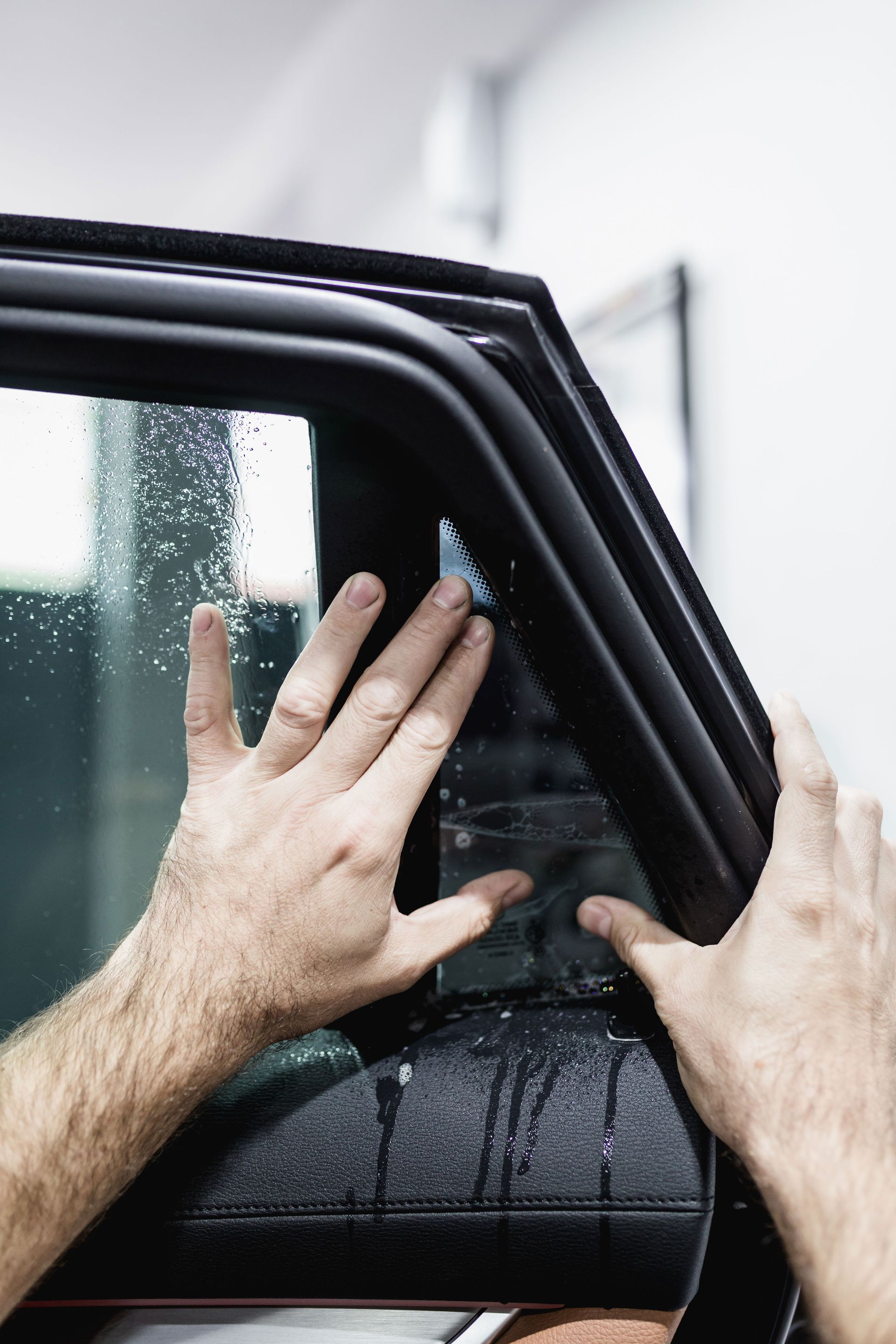 A person is applying tinted window film to a car window.