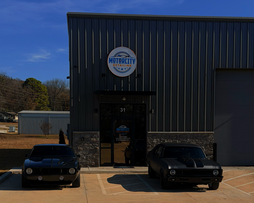 Two black classic cars parked in front of MotorCity Restorations building with a blue sign.
