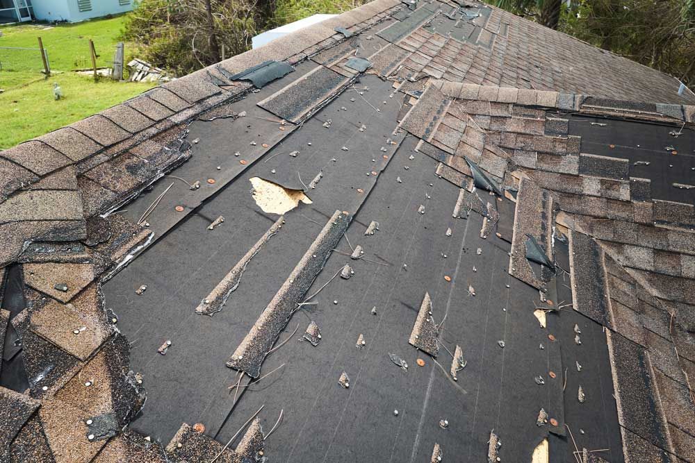 Damaged asphalt roof with missing shingles exposing the black underlayment and numerous nail heads.
