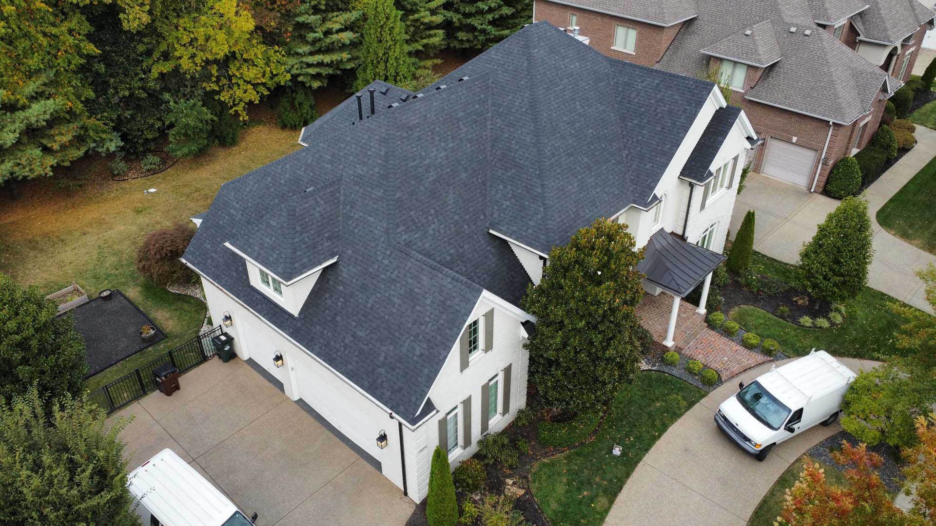 An aerial view of a white, two-story suburban house with a dark gray shingled roof, a paved driveway, and a white van.