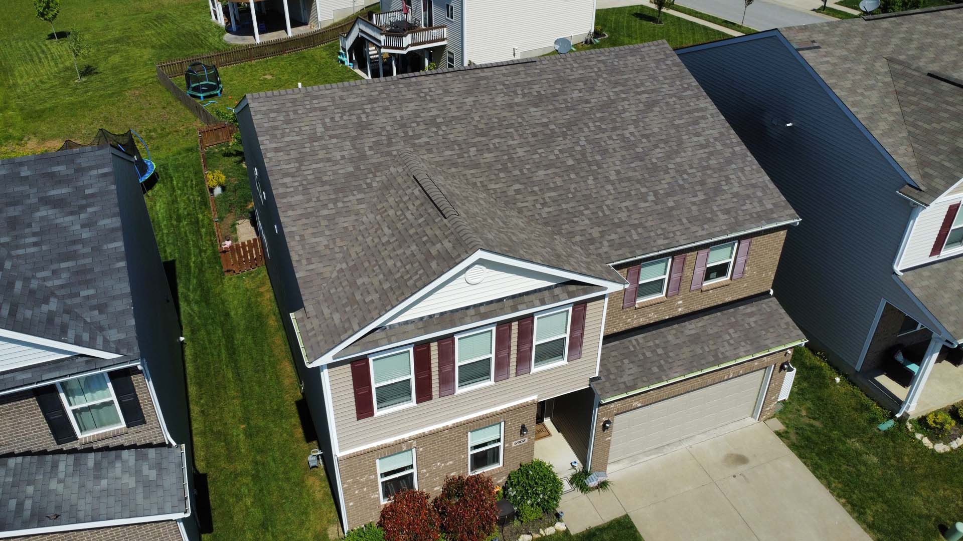 An aerial view of a two-story suburban house with a brown shingled roof, brick facade, and an attached two-car garage.