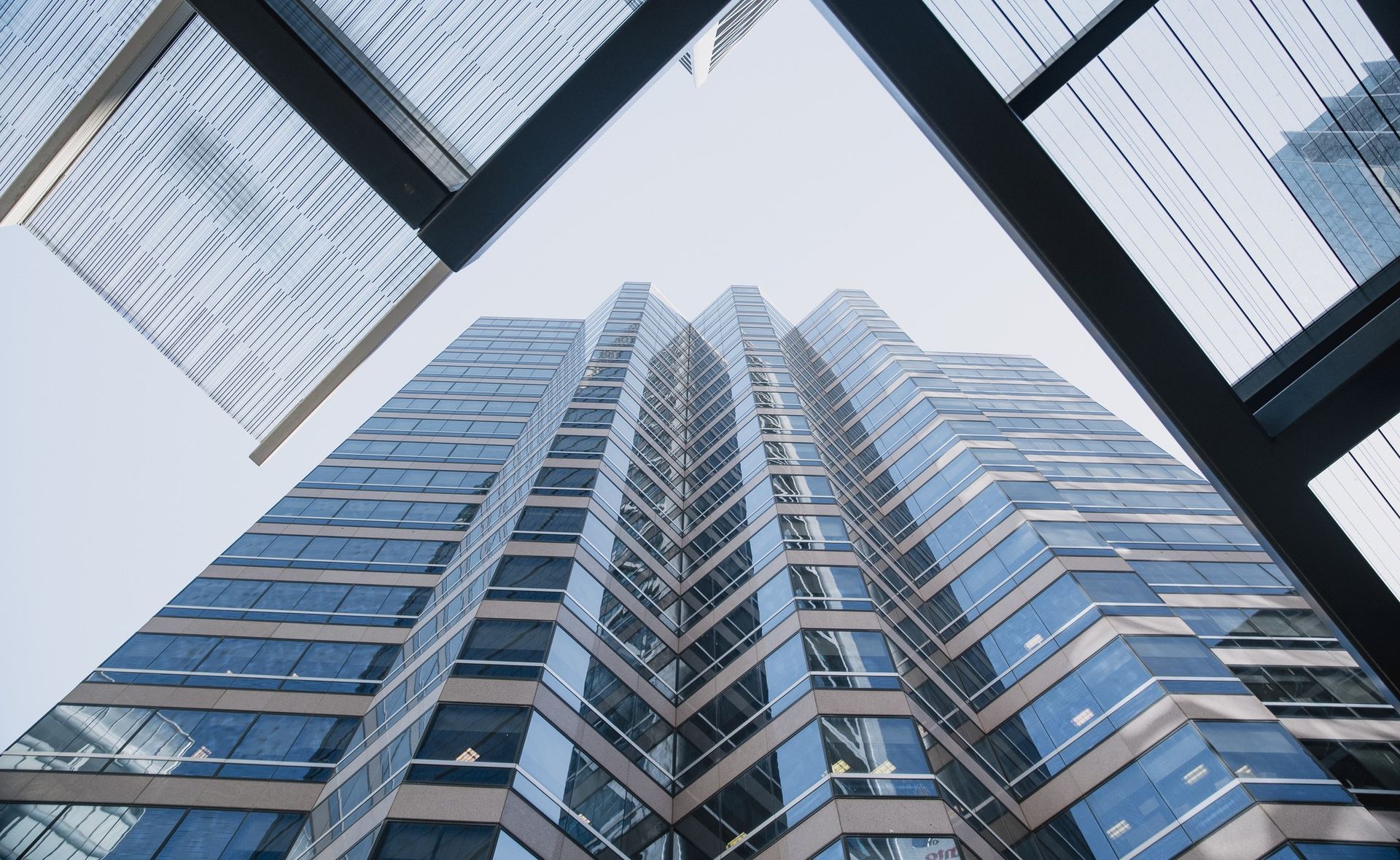 Low-angle view of a tall skyscraper with blue windows against a clear sky, viewed from below.