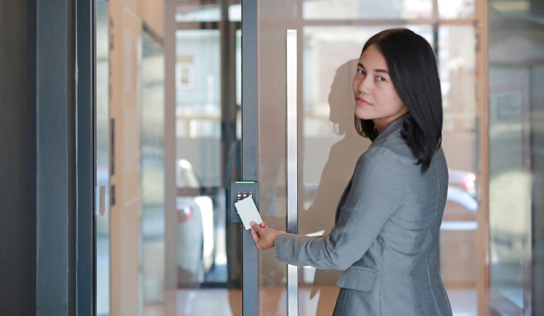 Woman in grey blazer uses ID card to open a glass door in an office.