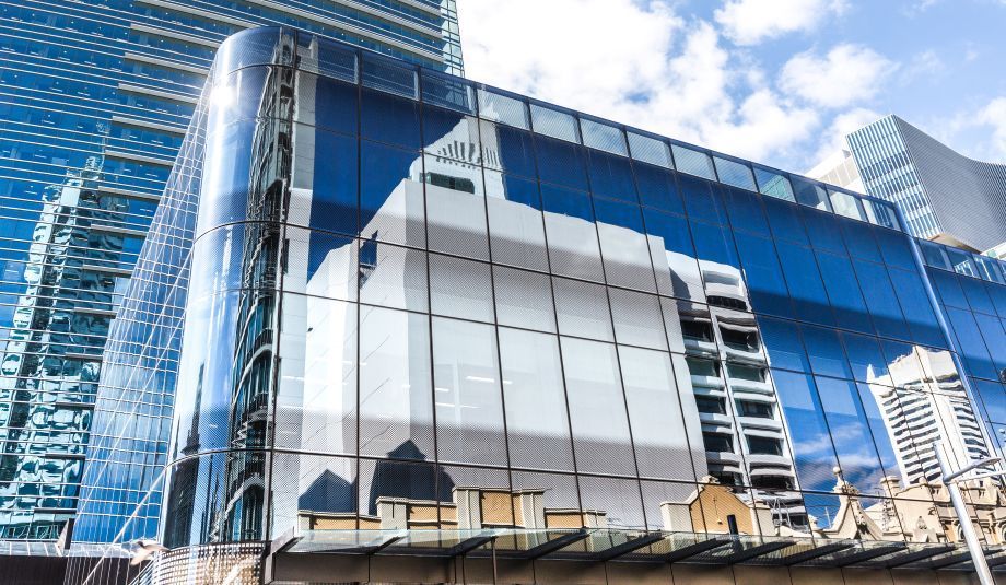 Modern glass building reflecting surrounding buildings under a blue sky - Perth