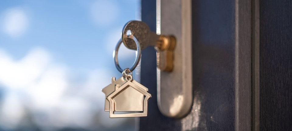 home security tips when on holiday: key in a lock with a house-shaped keychain, against a blurred blue sky background