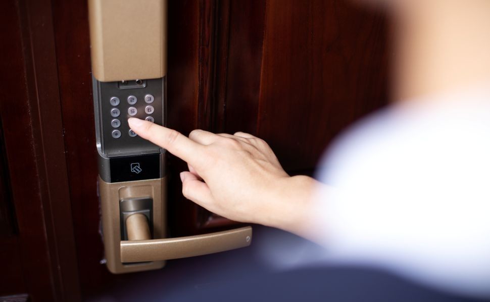 person's hand entering a code on a keypad entry door lock to unlock a wooden door.
