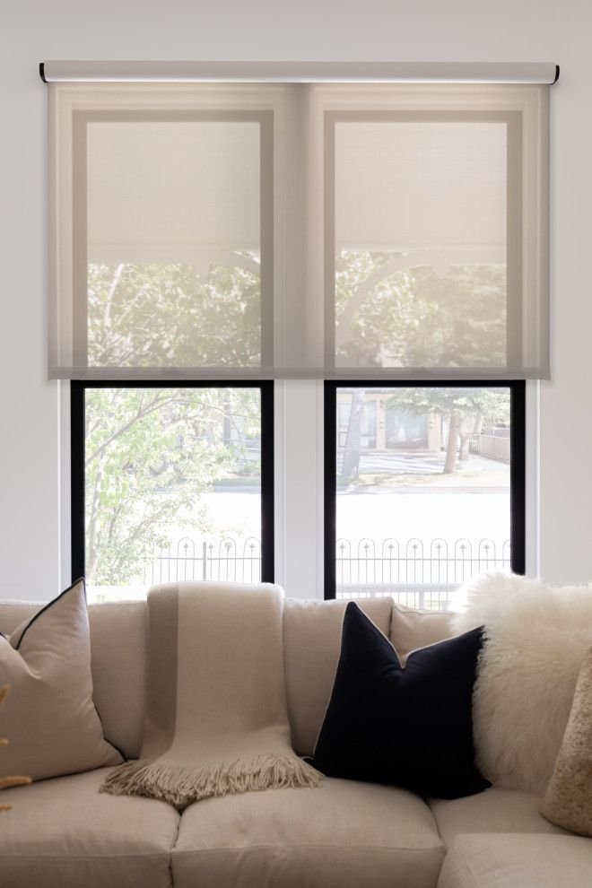 A living room with a couch and two windows with roller shades.