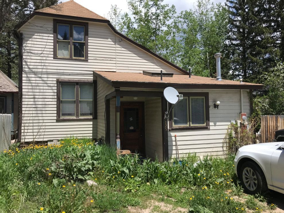 A white car is parked in front of a house with a satellite dish on the roof.