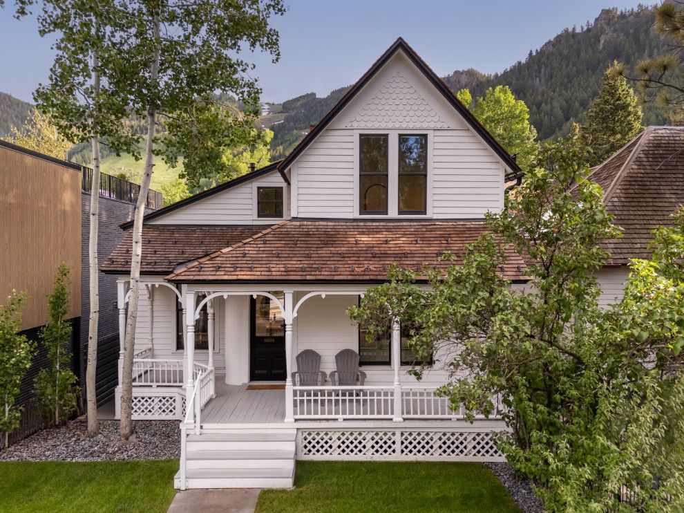 An aerial view of a white house with a porch and mountains in the background.