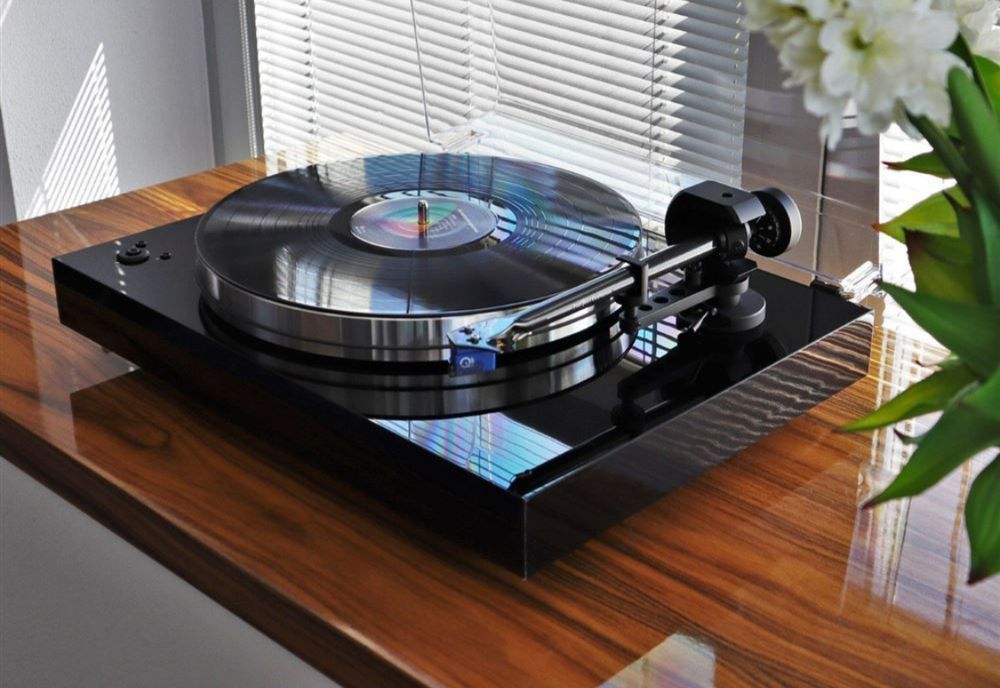 A record player is sitting on a wooden table next to a window.