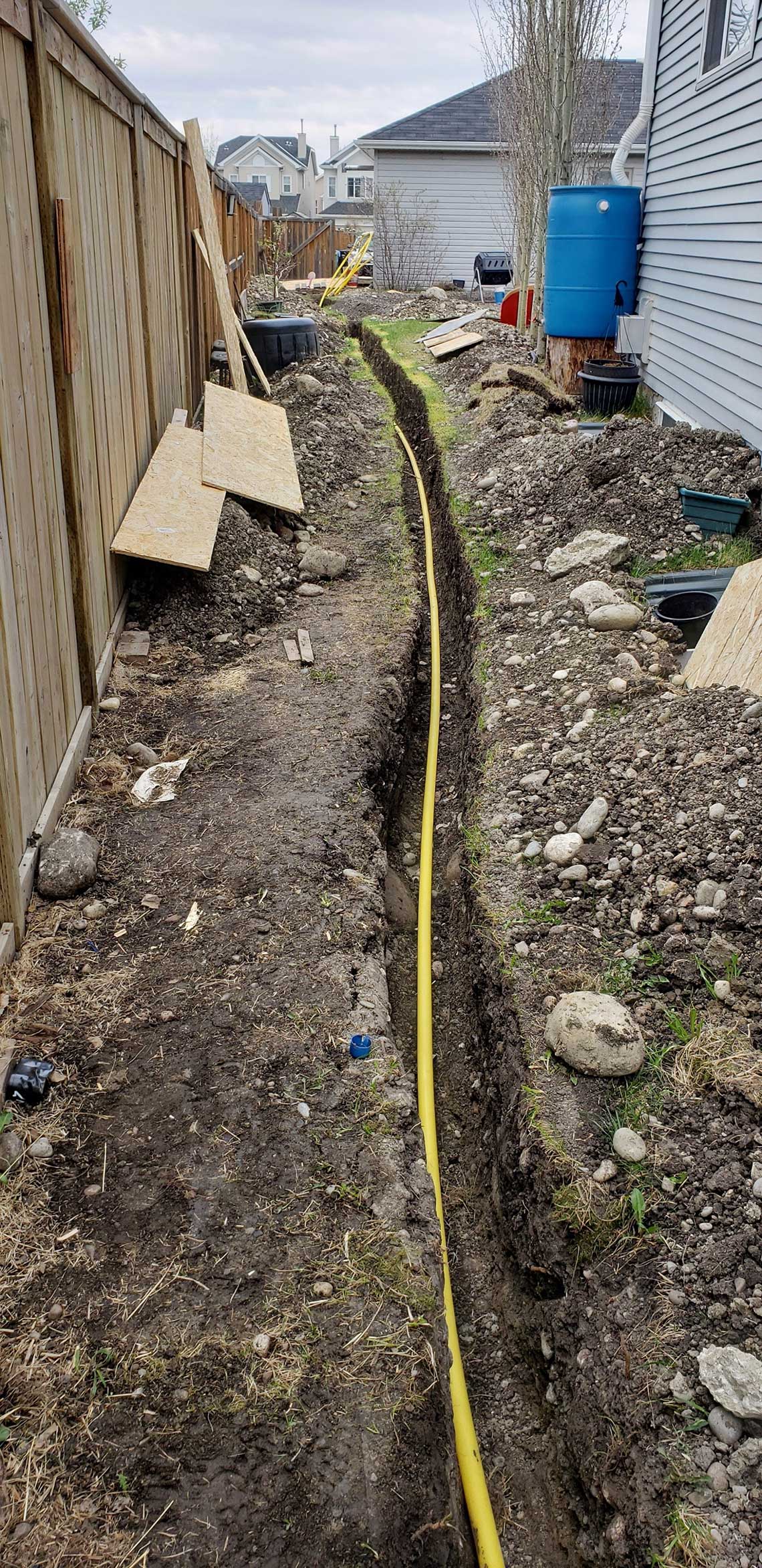 A yellow hose is laying in the dirt next to a fence.