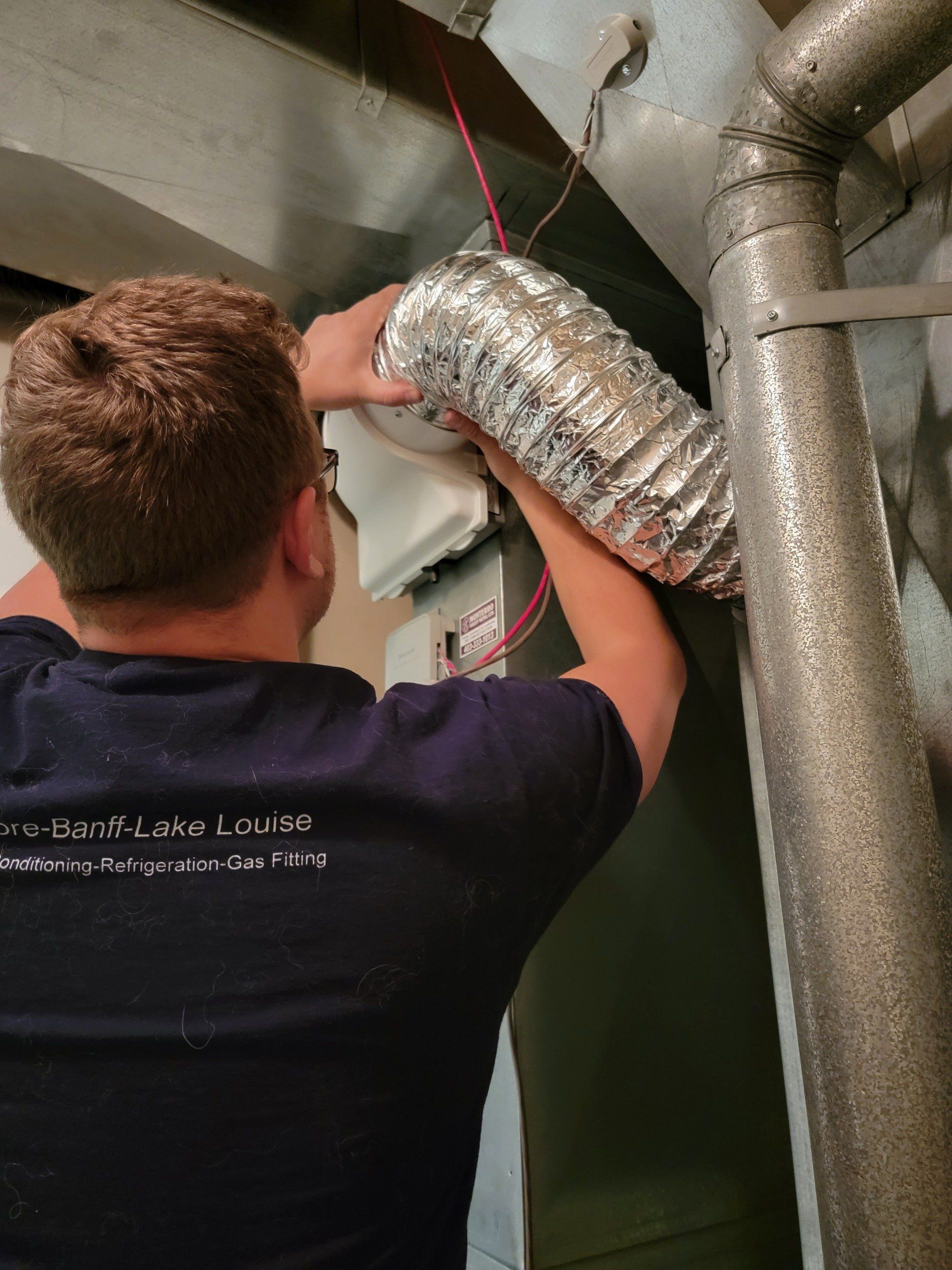 A man in a blue shirt is working on a duct