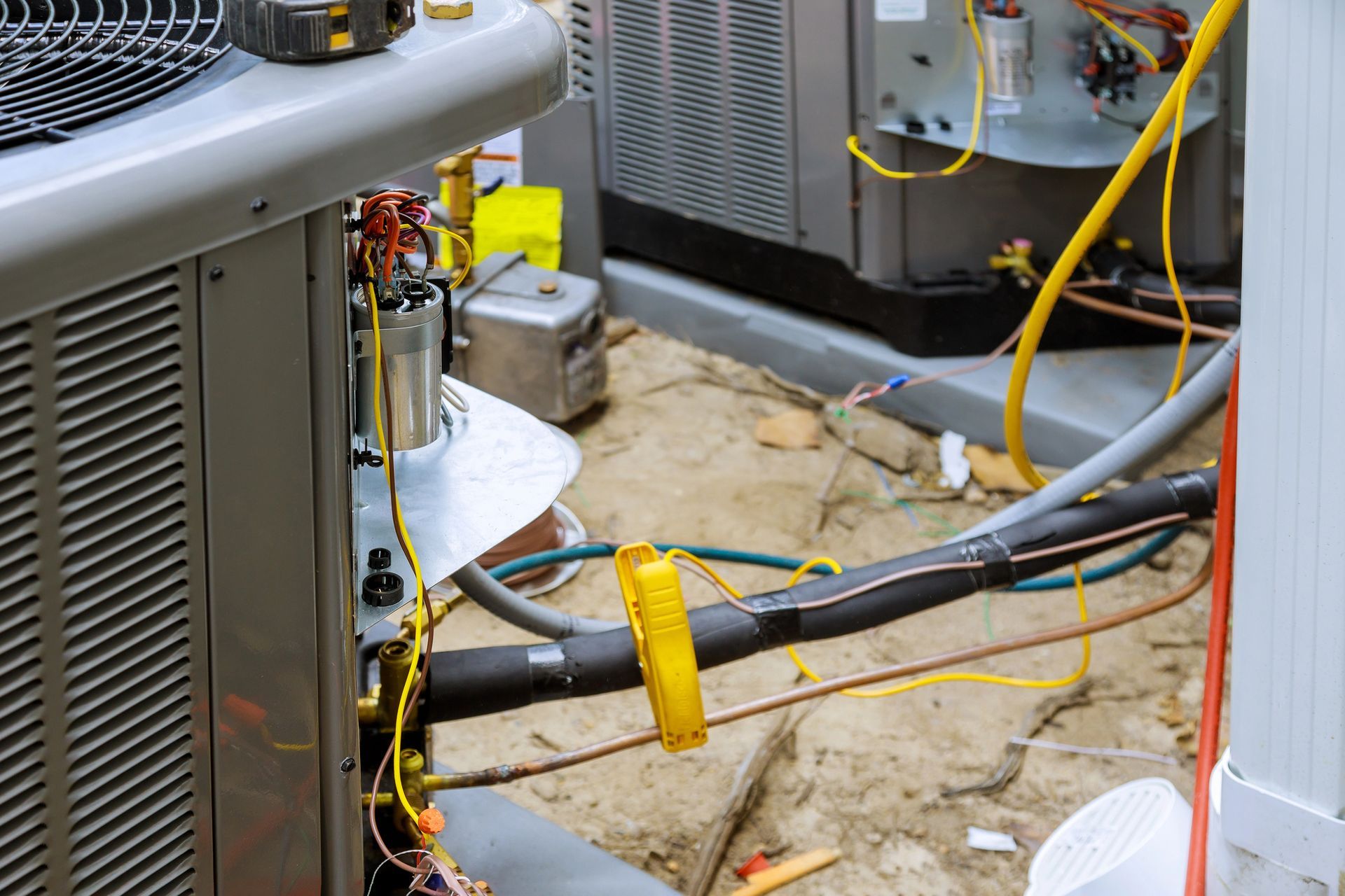 A technician's tool, a yellow clamp meter, is attached to an insulated coolant line on an outdoor HVAC unit.