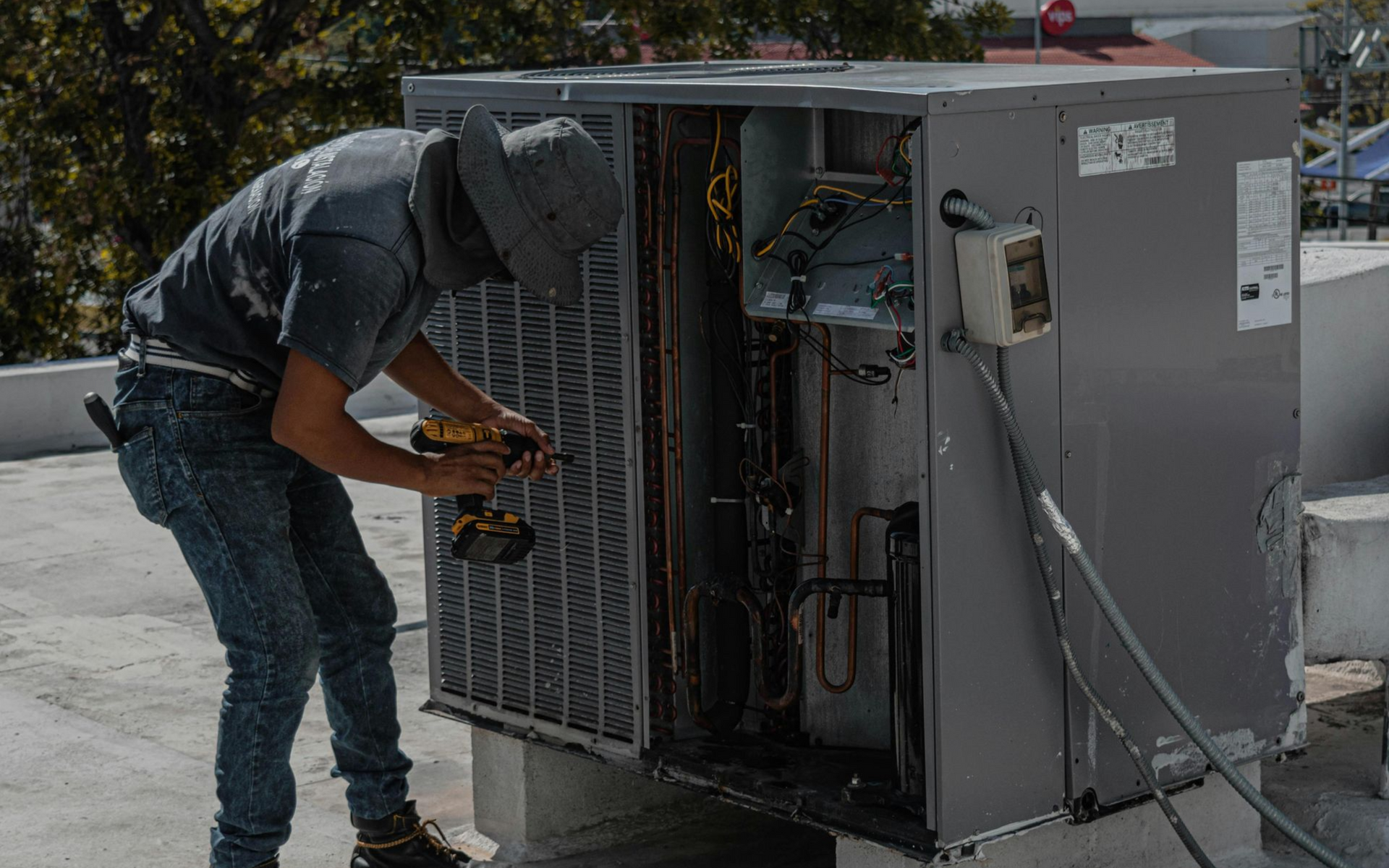 Person repairs an HVAC unit on a rooftop using a power drill.